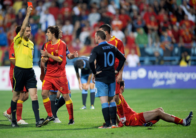 Wayne Rooneyt állítja ki a játékvezető Miodrag Dzudovic (földön) ellen elkövetett szabálytalansága után az Anglia-Montenegró (2-2) mérkőzésen