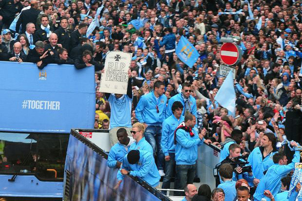 Carlos Tévez mutat fel  RIP Fergie feliratú táblát a Manchester City buszán, miközben a Premier League bajnoki címét ünnepli 2012-ben.