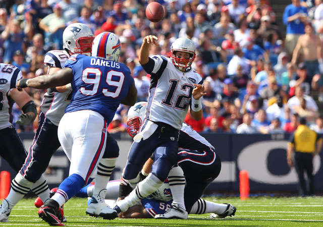 Tom Brady, a New England Patriots irányítója dobja el a labdát, miközben a Buffalo Bills egyik játékosa fogja meg a bokáját az NFL-ben 2011 szeptemberében