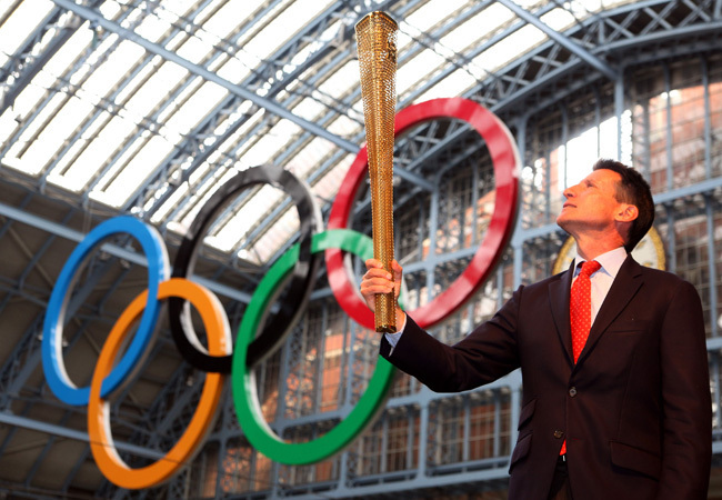 Sebastian Coe áll az olimpiát jelképező öt karika előtt a londoni játékok újonnan leleplezett fáklyájával a kezében 2011 júniusában