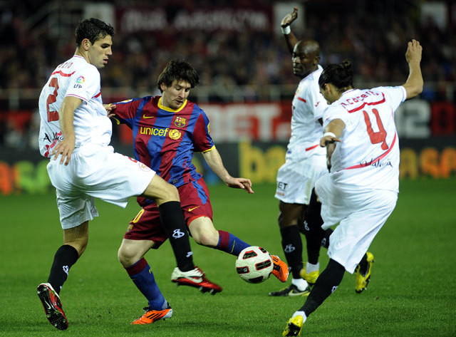 Lionel Messi a sevillai játékosok szorításában